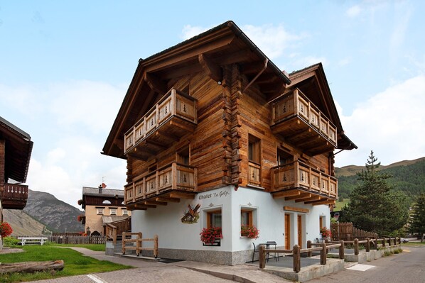 A wooden chalet with balconies, a sign reading 'Chalet 'la Gopa,' and a mountain backdrop.