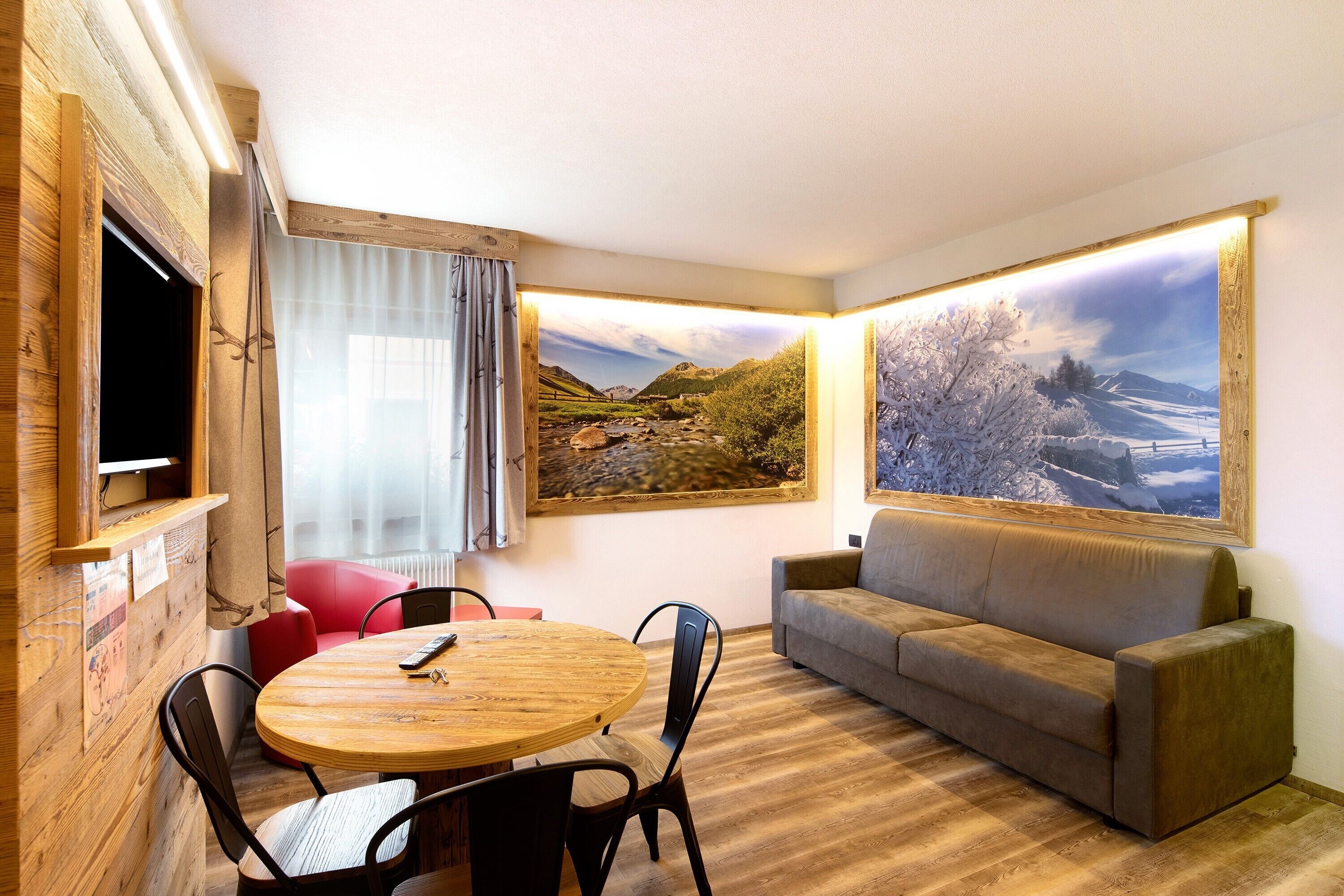 A room with a round wooden table, two chairs, a sofa, and two large landscape paintings on the walls.