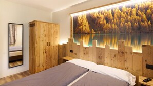 Een slaapkamer met een bed, een houten kledingkast, nachtkastjes en een groot schilderij van een bos en meer.
