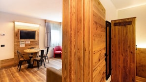 Een kamer met een houten wand, een televisie boven een houten tafel met stoelen, en een rode stoel op de achtergrond.