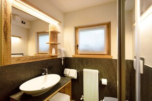 A bathroom with a large oval sink, a mirror, a towel rack, a window, and a shower area.