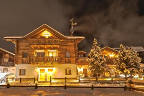 A snow-covered building with a balcony, a door, and a snow-covered tree in front.