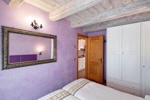 Un dormitorio con un espejo grande, vigas de madera en el techo, un armario y una puerta que da a un baño.
