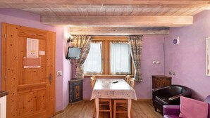 Ein Zimmer mit einem Holztisch, einem violetten Sofa, einem Fernseher und einem Fenster mit Vorhängen.