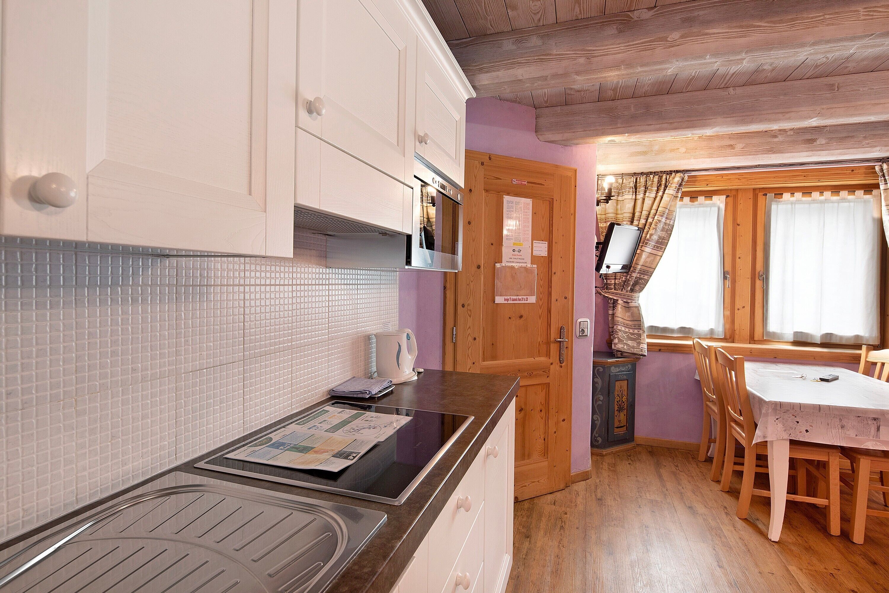 A kitchen with white cabinets, a microwave, and a stove. There is a dining area with a table and chairs, and a wooden door with a window.