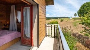 A wooden cabin with a balcony, a bed, and a view of the countryside.