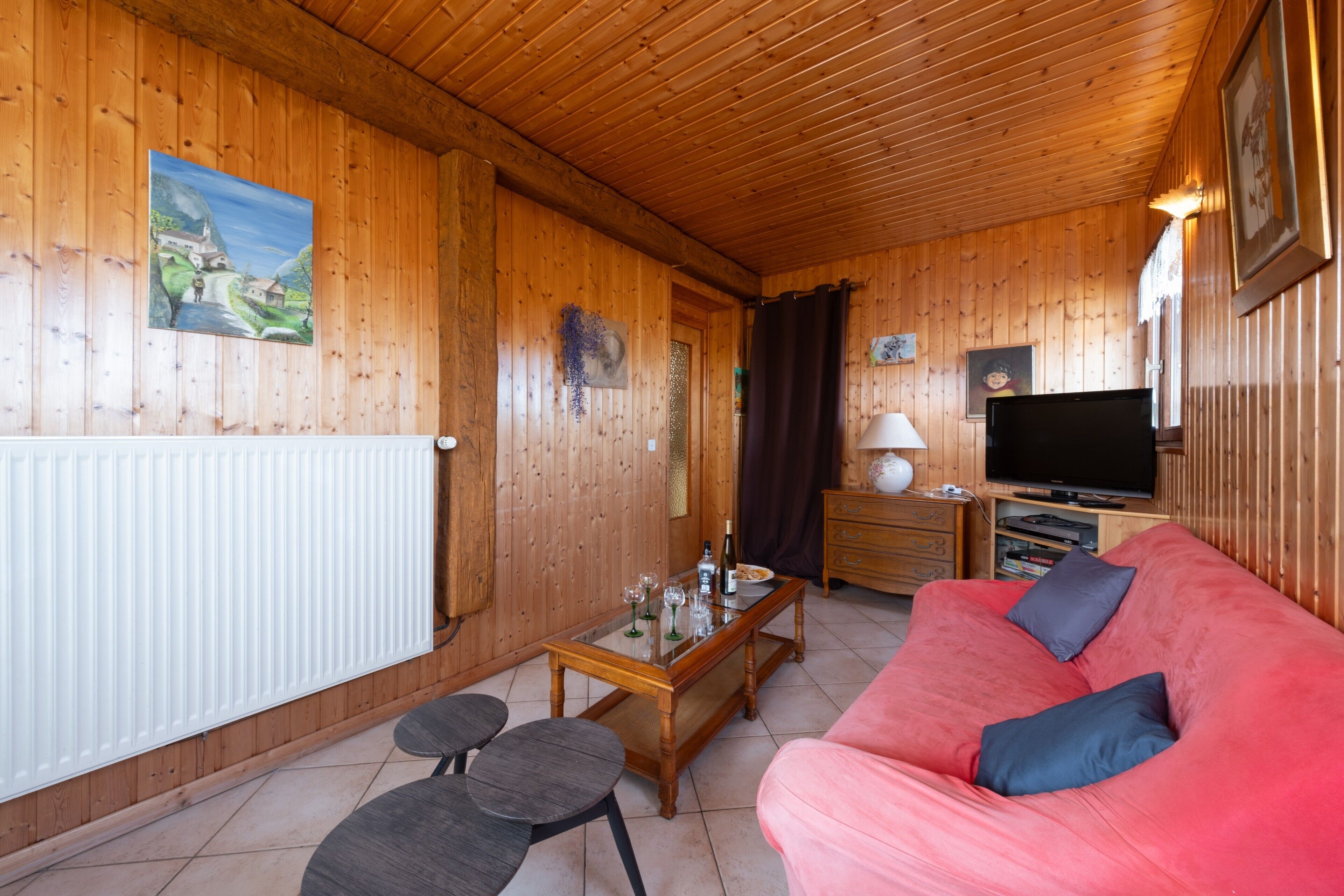 Un intérieur en bois avec un canapé rouge, un téléviseur et une table à manger avec des chaises.