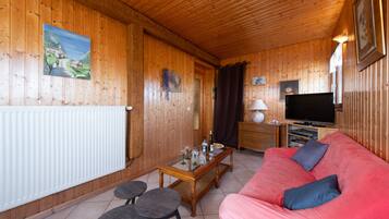 Un intérieur en bois avec un canapé rouge, un téléviseur et une table à manger avec des chaises.