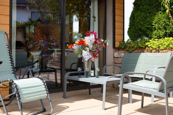 An outdoor seating area with metal chairs and tables, a vase with flowers, and a bottle of wine.