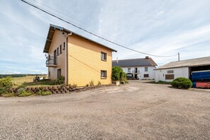 A yellow building with a balcony, a gravel driveway, and a white building with a garage in the background.