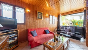 A wooden-paneled room with a red sofa, a television, and a glass table with snacks.