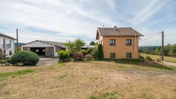 Une maison à deux étages avec un garage, entourée d’une cour verdoyante et de quelques arbres.