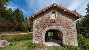A stone structure with a pitched roof, an arched entrance, and a bench inside.