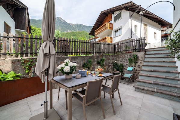 A patio with a table, chairs, and a covered umbrella. There is a staircase leading to a second floor.