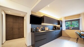 A modern kitchen with dark cabinetry, a flat-screen TV, and a window with a view of greenery. - Apartment "Maja" with Mountain View, Private Garden and Wi-Fi (San Martino In Passiria)