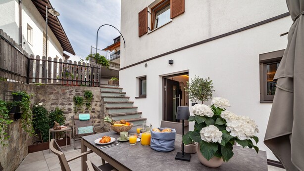 A patio with a table set for breakfast, outdoor seating, and a staircase leading to an upper level. - Apartment "Maja" with Mountain View, Private Garden and Wi-Fi (San Martino In Passiria)