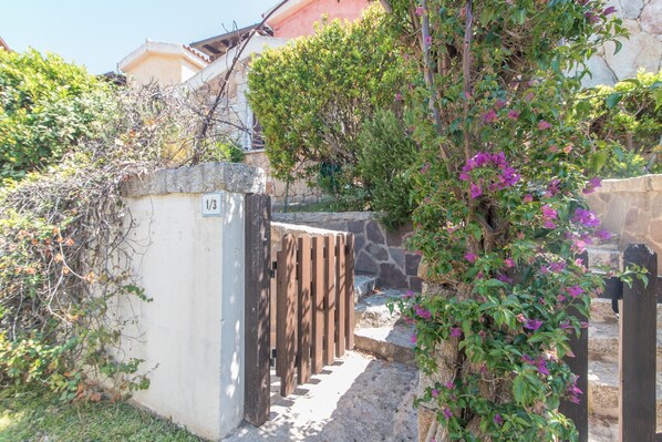 A stone wall with a wooden gate, a stone staircase, and a bush with purple flowers.