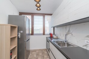 A compact kitchen with a built-in refrigerator, a sink, and a window with blinds.