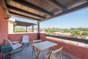 A balcony with a wooden ceiling, a table, and two chairs.