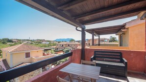 Un balcone con tavolo e sedie, affaccia su una zona residenziale con case e montagne.