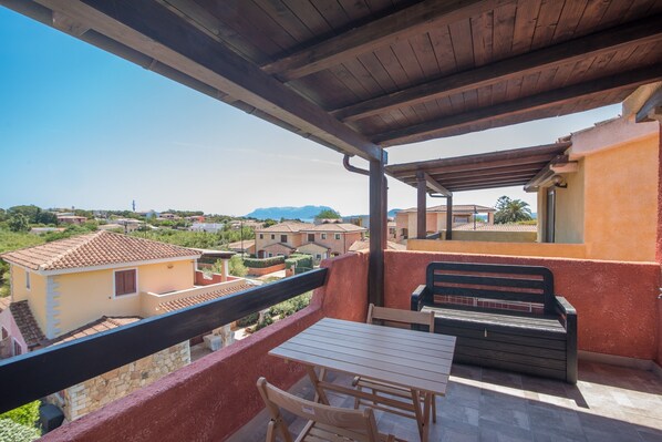 A balcony with a table and chairs, overlooking a residential area with houses and mountains.