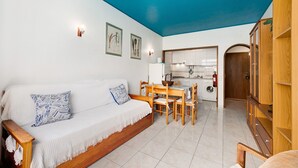 Una sala de estar con sofá, mesa de comedor, sillas y una cocina al fondo.