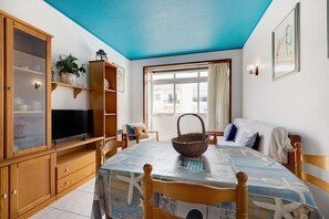 A room with a dining table, wooden cabinets, a television, and a window with curtains.