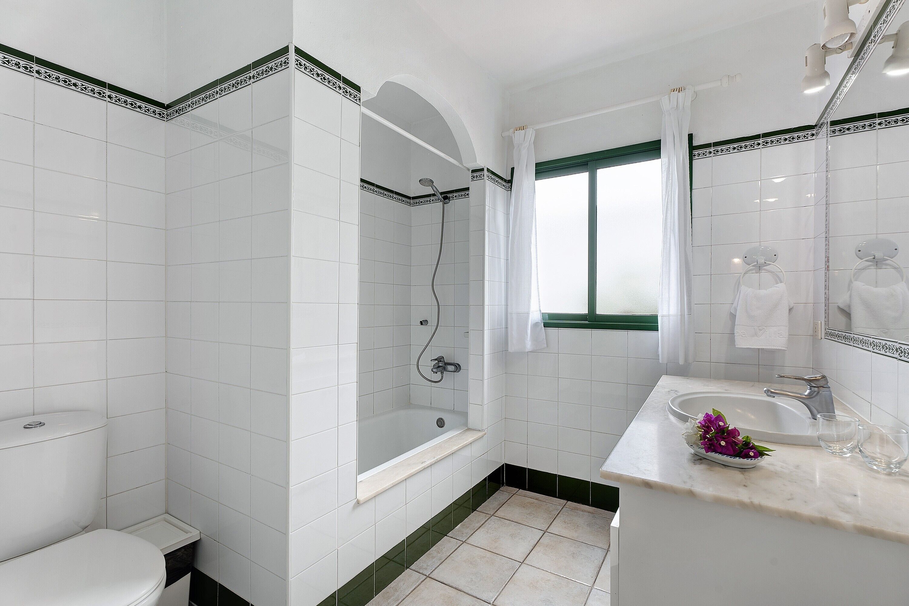Un baño con azulejos blancos, una bañera, un inodoro, un lavabo y un espejo.