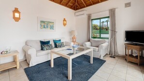 Un salon avec un plafond en bois, des murs blancs, un canapé, une table basse, un téléviseur et une fenêtre donnant sur un beau paysage.
