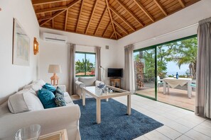 A living room with a sofa, coffee table, TV, and a view of the outdoors. - Holiday Home 'La Villa La Palma - 1 Dormitorio' with Sea View, Wi-Fi and Air Conditioning (Dos Pinos)