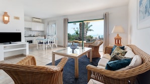 Una sala de estar con muebles de mimbre, una mesa de centro de vidrio y un televisor.