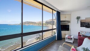 Una stanza con un'ampia finestra vista spiaggia, un divano rosso, un piccolo tavolino bianco e un armadio.