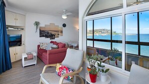 Un soggiorno con un divano rosso, una poltrona bianca, una TV e un'ampia finestra vista mare.