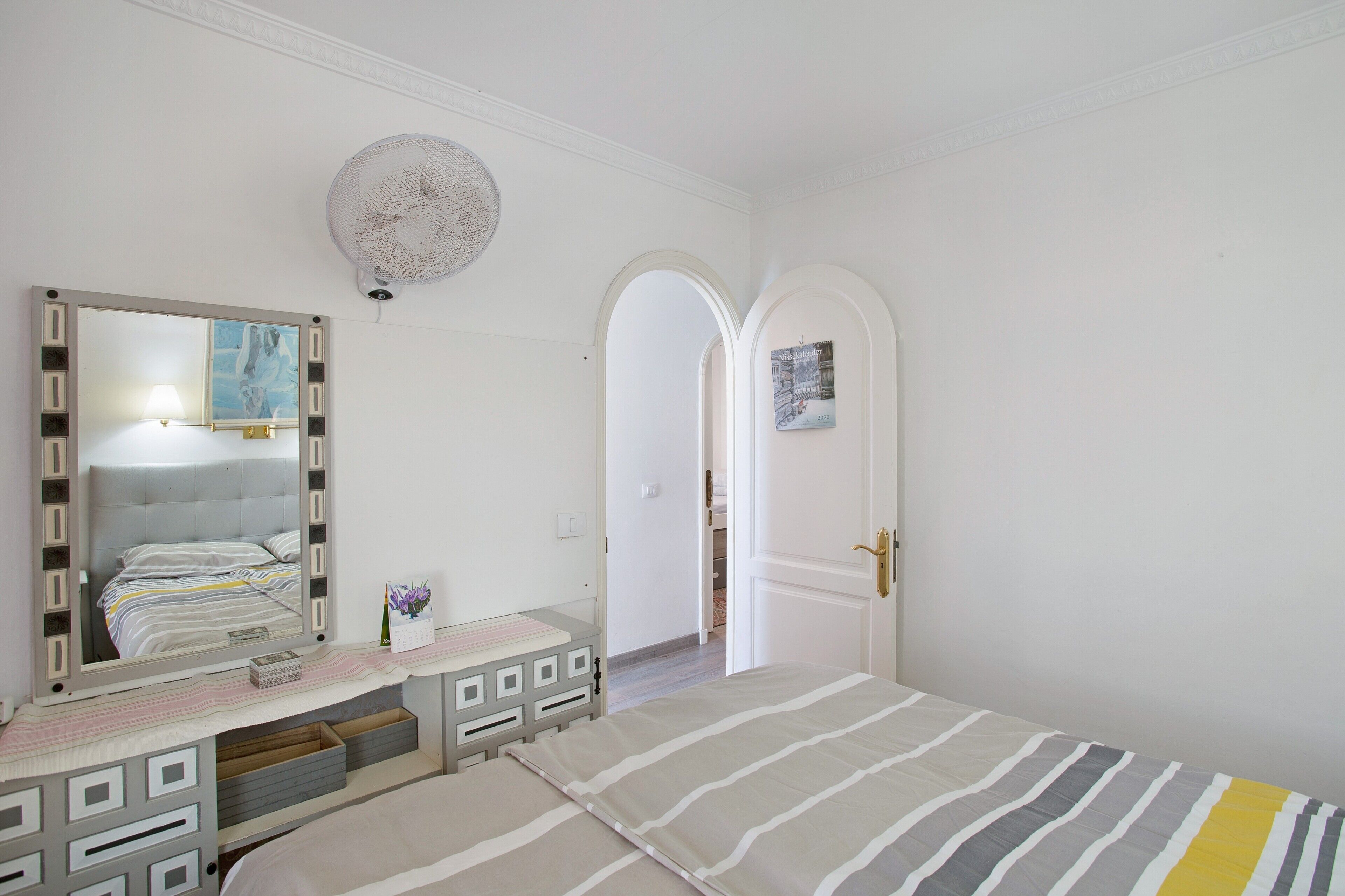 Une chambre à coucher avec un lit, une commode, un miroir et une porte en arc de cercle.
