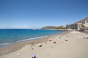 Une plage avec un hôtel en arrière-plan, un ciel dégagé et l’océan.