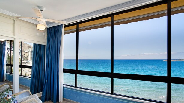 Una stanza con un'ampia finestra, un ventilatore a soffitto e vista sull'oceano.