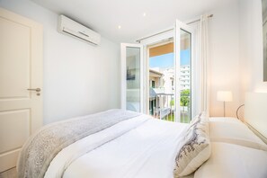 Un dormitori amb un llit, una porta oberta que dona a un balcó i un aparell d'aire condicionat a la paret.