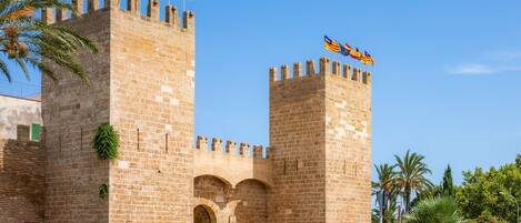 A historic stone castle with two prominent towers, a central arched entrance, and flags on top.