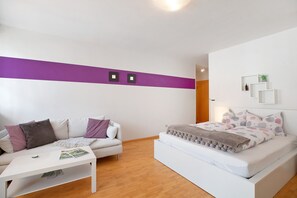 Une chambre moderne avec un canapé, un lit, une table basse et une petite plante.