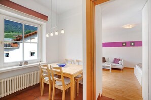 Une pièce comprenant une table à manger, des chaises, un radiateur, une fenêtre donnant sur une maison et des montagnes, un canapé et un lit.