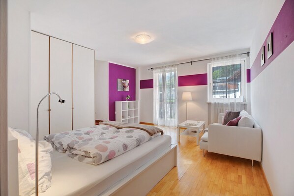 Une chambre à coucher moderne avec un lit, un canapé blanc, une petite table et une fenêtre avec des rideaux.