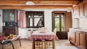 A wooden kitchen with a dining table, cabinets, and a window with curtains. - Holiday Apartment "Genzianella Tano Di Grich" with Mountain View & Private Terrace (San Michele Prazzo)