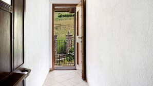 A narrow hallway leading to a balcony with a view of a garden and a stone structure. - Holiday Apartment "Genzianella Tano Di Grich" with Mountain View & Private Terrace (San Michele Prazzo)