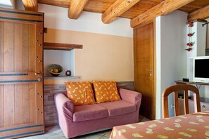 A cozy room with a wooden door, a pink sofa with patterned cushions, a small table, and a television.
