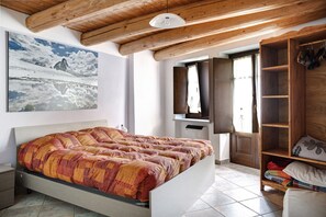 A bedroom with a bed, wooden ceiling beams, a large window, and a wardrobe.