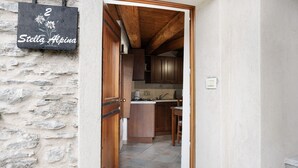 A narrow hallway leading to a kitchen with wooden cabinets and a stone wall.