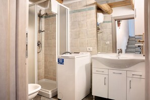 A bathroom with a shower, toilet, and washing machine.