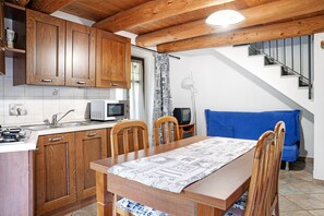 A kitchen with wooden cabinets, a dining table with chairs, a microwave, and a staircase leading to a living area.