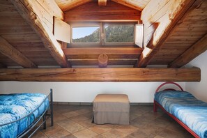 Un dormitorio con techo inclinado, dos camas, un taburete pequeño y una ventana con vista a la montaña.
