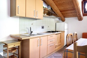 A kitchen with wooden cabinets, a sink, a stove, and a dining area with chairs. - Holiday Apartment 'Anemone Tano Di Grich'"with Mountain View, 2 Balconies & Shared Terrace (San Michele Prazzo)